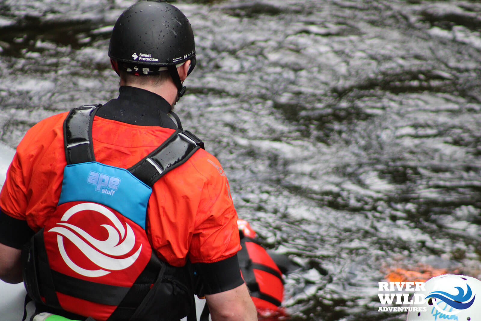 A photo of a rafting guide wearing a red jumpsuit facing back to the camera, wearing a helmet